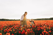 An art therapist leads a girl with Down syndrome by the hand through a field of poppies at sunset