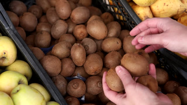 Close-up of many kiwis in trading baskets and a male hand takes one.