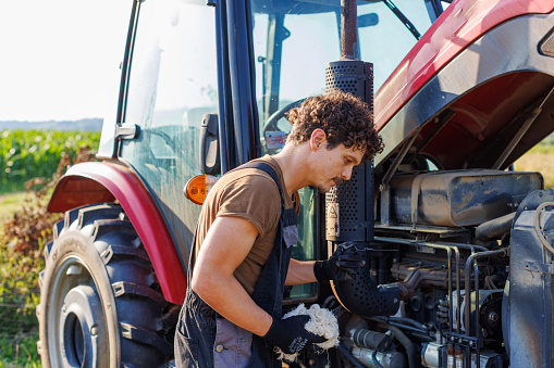A farmer or mechanic performs routine maintenance on his tractor before harvest.