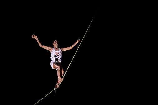 Certaldo, Italy - 2023, Jul 12: Tightrope walker walking and balancing on the wire at MERCANTIA International Street Theater Festival. Black background. Copy space.