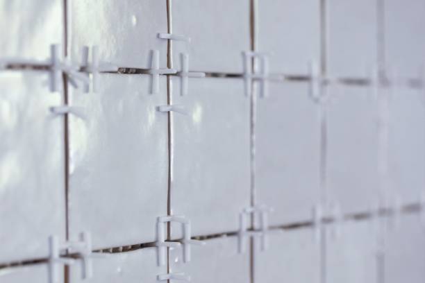 A portrait of a tile wall under construction. The wall is being tiled with small bumpy rectangular tiles. There are still white plastic joint spacers in between the junctures of the ceramic tiles. un retrato de una pared de azulejos en construcción. la pared está siendo embaldosada con pequeños azulejos rectangulares llenos de baches. todavía hay espaciadores de juntas de plástico blanco entre las uniones de las baldosas cerámicas.