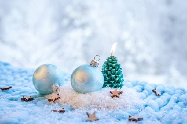 istock Christmas products background. Blue frosty pattern baubles on snow with green spruce tree shape candle burning. Bokeh snowy winter forest background. 1561109916