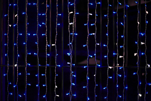 Christmas garlands decorated with white vertical curtains and white and blue round lights, isolated against the black background.