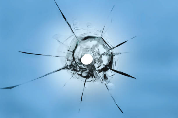istock A hole from a weapon hitting the glass. Cracked window on a blue background. 1561125560