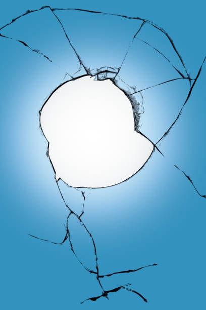 istock Big hole in window glass blue and white background background. Broken glass with cracks. 1561126438