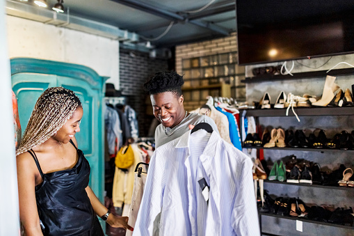 Young adult African couple choosing dress at second hand sale stock