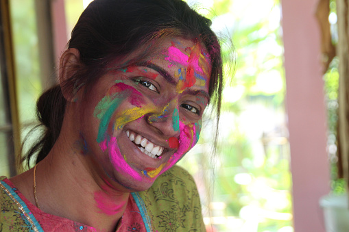 An Indian lady in 30s with face full of vibrant colours and looking towards the camera and smiling-Holi concept image