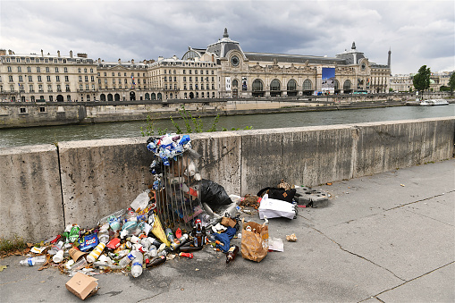 Paris, France-07 15 2023: Trash can overflowing on the banks of the Seine river in Paris with a view of the Musée d'Orsay, France.