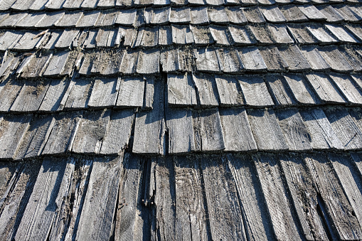 Wooden gray roof shingles. Wood weathered roofing pattern detail. Old grey wooden roof texture. Old shabby wooden tiles close-up background.