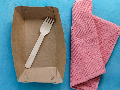 Empty paper plate and wooden fork on a blue background. Eco friendly materials. Diet for weight loss, weight loss. Food restrictions. Disposable paper tableware. Plastic free and zero waste concept.