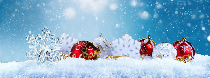Beautiful Christmas panoramic background with snowflakes and Christmas red and white balls in snow against blue sky and snowfall. New Year congratulatory banner.