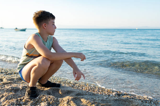 istock Thoughtful sad boy is crouching alone at the beach. 1561232894
