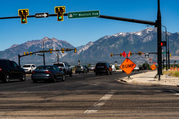 Amidst a sunny summer day in the suburbs, vehicles pass through an intersection, revealing the sprawling cityscape and distant mountains.