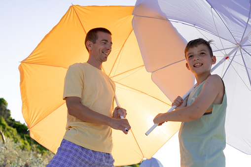 Father and son with beach umbrellas on tropical beach vacation. Happy, smiling family who enjoy summer day at the beach.