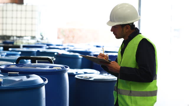 Latin American man supervising the operation of a chemical plant and taking notes on a clipboard