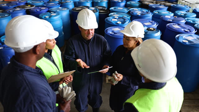 Latin American mature leader of a diverse team in a chemical plant talking to his team and listening