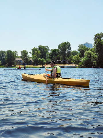 Kayaking A young guy is canoeing on a wide river and smiling. Side view. Sports tourism and active leisure in beautiful summer nature