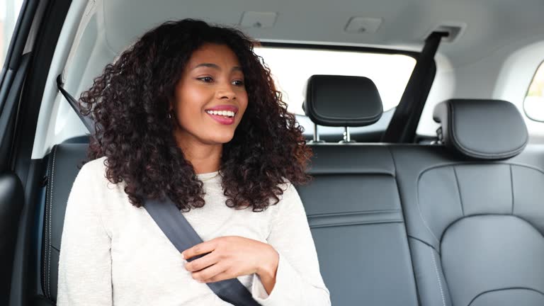 African-American getting into a crowdsourced taxi fastening her seat belt while greeting very cheerfully and smiling