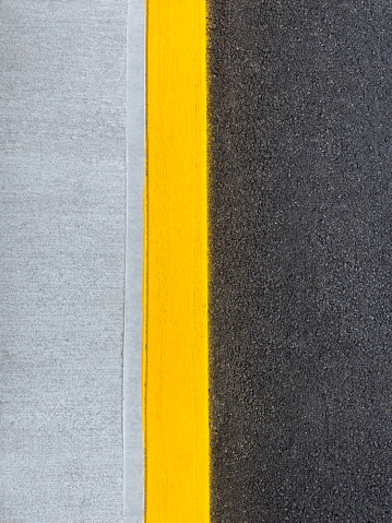 Looking down on a concrete sidewalk with yellow marking and asphalt