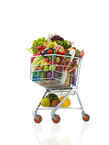 Faceless woman in denim shirt standing in supermarket with shopping cart full of healthy food