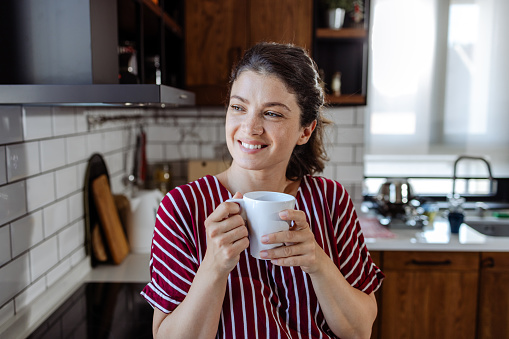 Woman in her mid 30s, relaxing in the kitchen and enjoying her morning coffee