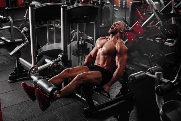 istock Muscular bodybuilder man using weights machine for legs at the gym. Hard training 1561412581