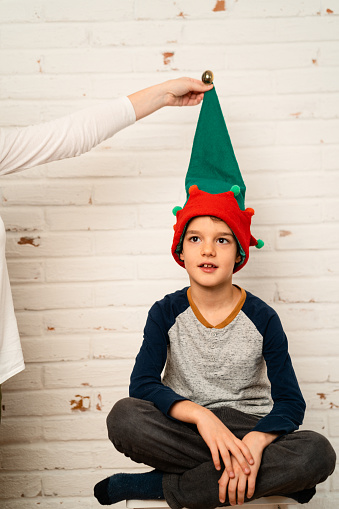 Little boy posing with elf hat against white brick wall for a greeting Christmas card