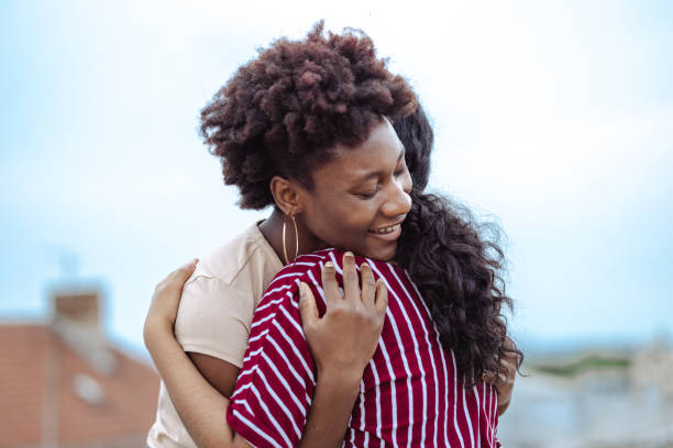 Two young female friends exchanging an affectionate hug on a rooftop stock photo
