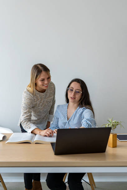 istock Two smiling businesswomen working in office with laptop computer. 1561448123