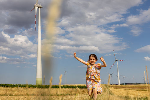 Happy four years old girl is running near wind generator