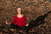 A woman with cancer meditating on a meadow with dry leaves during a sunset.
