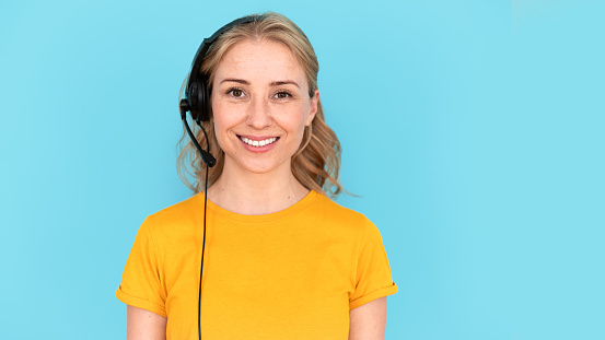Concept of customer support and call centre for clients. Portrait of happy personal assistant in headset standing isolated on blue copy space background. Female operator smiling, looking at camera