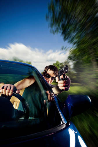 Crossprocessed portrait of a man driving a sports car and shooting with a handgun through the window.