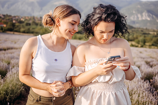 Friends sending text message using mobile phone while standing in lavender field