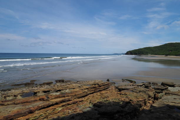 El Coco Beach, Nicaragua. Playa El Coco, Nicaragua, on a sunny summer day showing its beach, rocks, vegetation and cloudscape. el coco stock pictures, royalty-free photos & images