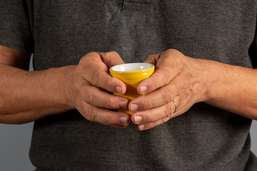 Hands of an elderly man holding a mug with a hot drink. Cup of coffee or tea