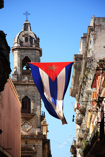 Cuban flag flapping in the breeze between old, historic buildings in Havana with a church in the background (350dpi)