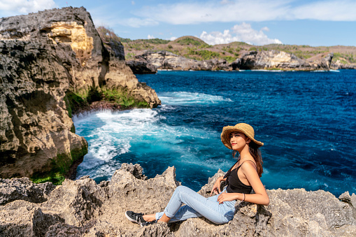 Indonesian girl take selfie by a smartphone at Broken Beach, located in Nusa Penida Island, the southeast island of Bali, Indonesia. The amazing tourist attraction of the rock