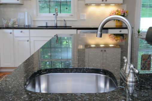 Modern stainless steel faucet and sink on kitchen island. Elegant granite counter.