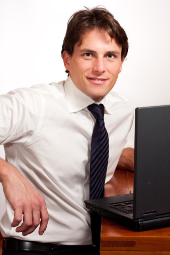 Attractive, smiling businessman at computer. Looking at camera.