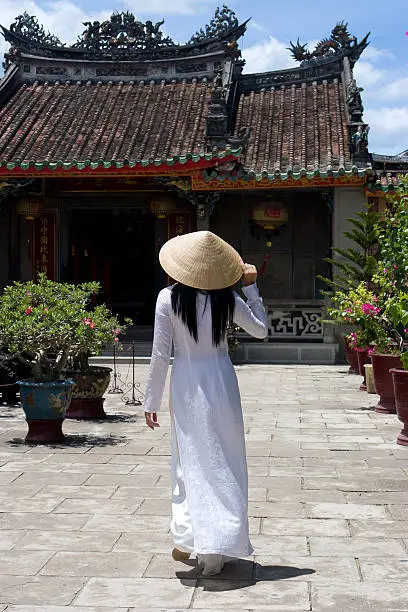 Vietnamese Woman wearing a traditional Ao-Dai costume in front of a Temple