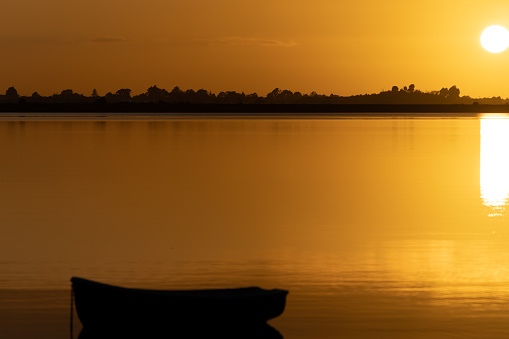 Golden sunrise with glow of round sun rising above horizon across bay.