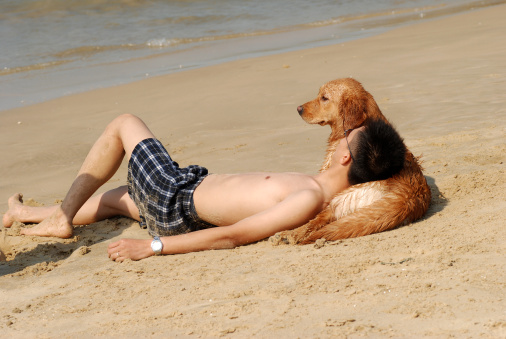 Man lying against his dog on the beach