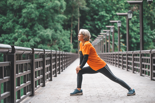 Elderly, white-haired Asian woman exercising in the park early in the morning.