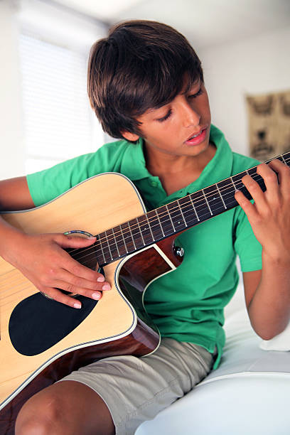 Young boy playing guitar on bed stock photo