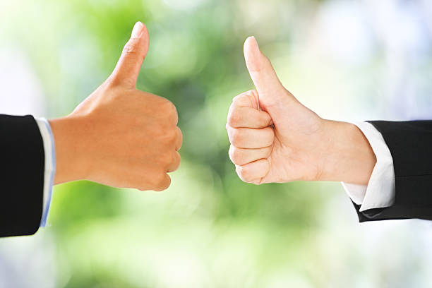 People raise thumbs up in line with green environment background. DIfferent skin tones and shallow depth of field