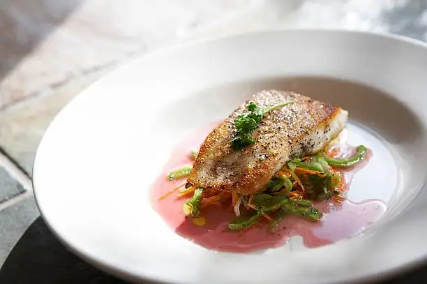 Grilled white fish with garnish served over vegetables on white plate