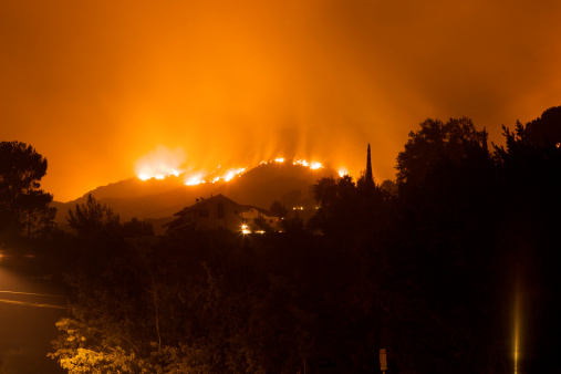 A raging fire burns on a hillside, threatening homes in a residential neighborhood.