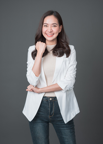 Smiling asian businesswoman standing with arms folded and looking at camera isolated over gray background. Successful