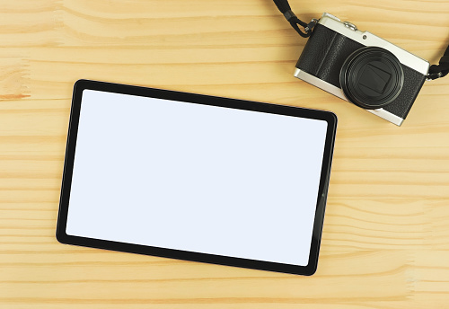 Top view or flat lay of digital tablet with blank white screen and digital camera isolated on wooden table background.